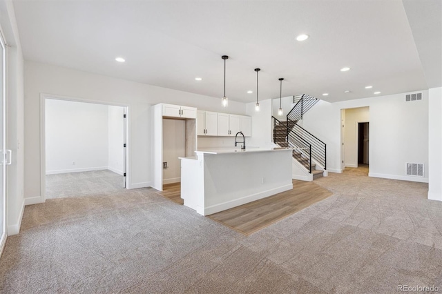 kitchen with pendant lighting, white cabinetry, sink, a center island with sink, and light carpet