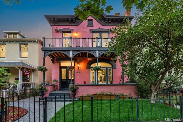 italianate house featuring a fenced front yard, a front yard, brick siding, and a balcony