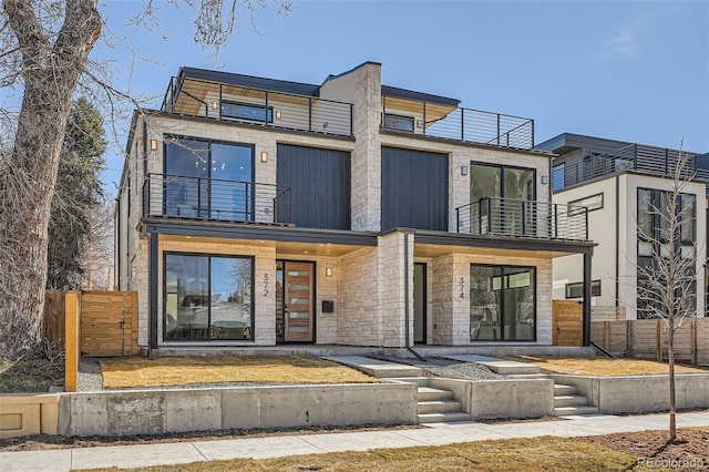 contemporary house with stone siding, a balcony, and fence