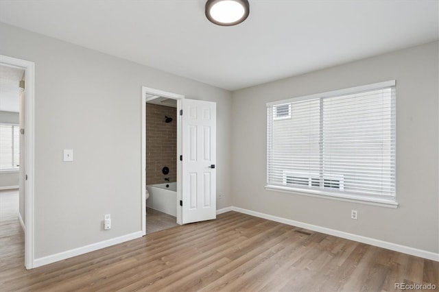 unfurnished bedroom featuring light hardwood / wood-style floors, a walk in closet, and ensuite bathroom