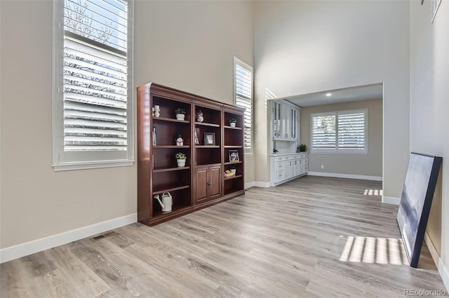 unfurnished living room with baseboards, light wood-style flooring, and a towering ceiling
