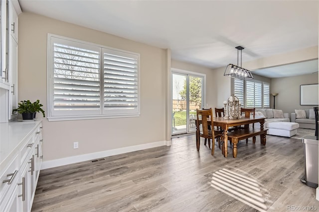 dining room featuring baseboards, visible vents, light wood-style flooring, and an inviting chandelier