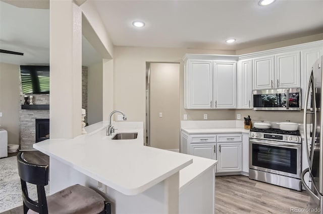 kitchen featuring a peninsula, a breakfast bar, white cabinets, a sink, and appliances with stainless steel finishes