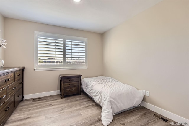 bedroom with baseboards, light wood finished floors, and visible vents
