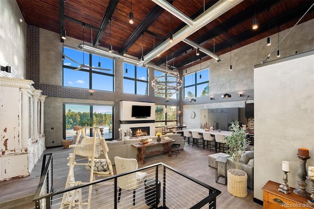 living room featuring a warm lit fireplace, wood ceiling, wood finished floors, a high ceiling, and track lighting