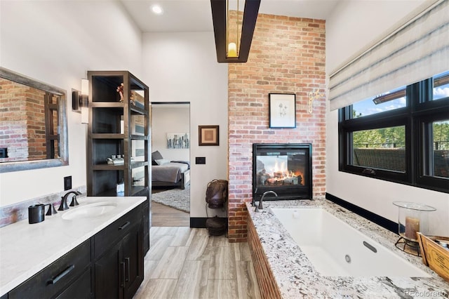 ensuite bathroom featuring ensuite bathroom, a fireplace, wood finished floors, vanity, and a whirlpool tub