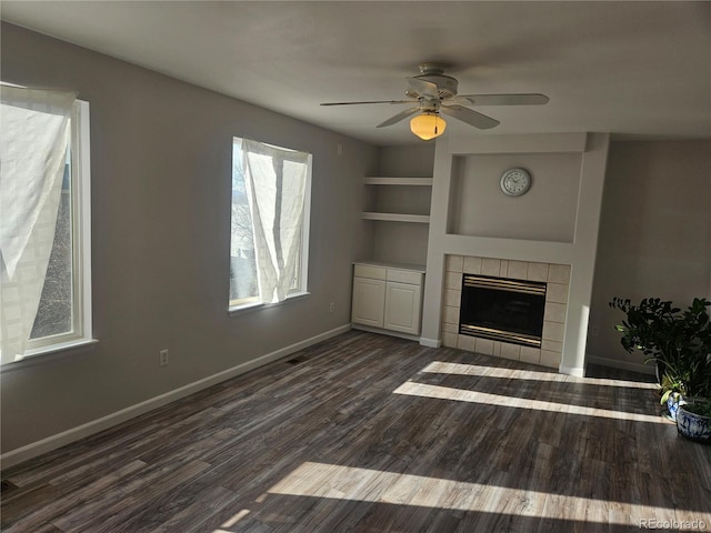 unfurnished living room featuring built in features, a tile fireplace, dark hardwood / wood-style floors, and ceiling fan