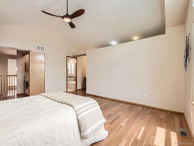 bedroom with vaulted ceiling, light wood-style floors, washing machine and clothes dryer, baseboards, and ensuite bath
