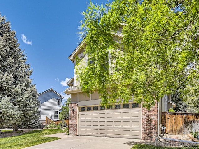 view of property hidden behind natural elements featuring brick siding, driveway, fence, and a garage