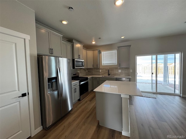 kitchen with gray cabinetry, dark hardwood / wood-style flooring, a kitchen island, stainless steel appliances, and backsplash