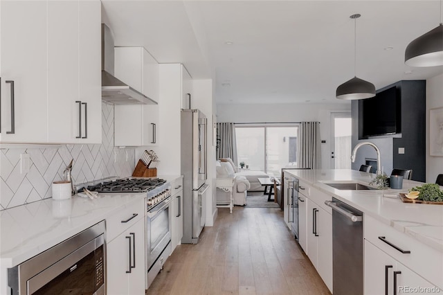 1322 Raleigh St, Denver, CO 80204 - kitchen featuring wall chimney range hood, white cabinets, appliances with stainless steel finishes, a sink, and open floor plan