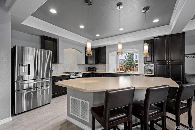 kitchen featuring appliances with stainless steel finishes, a raised ceiling, light wood-style flooring, decorative backsplash, and recessed lighting