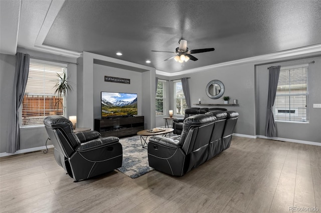living room featuring a textured ceiling, ceiling fan, light wood-type flooring, baseboards, and ornamental molding