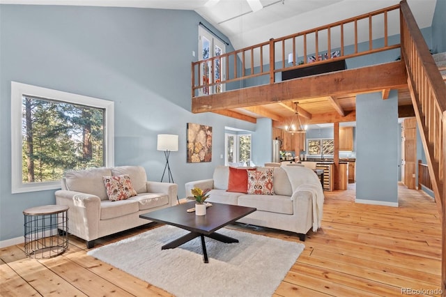 living room featuring vaulted ceiling with beams, light wood-type flooring, a wealth of natural light, and a notable chandelier