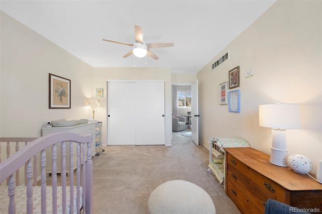 bedroom with a closet, visible vents, light carpet, ceiling fan, and a crib