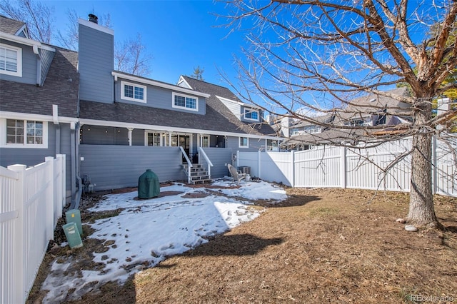 snow covered back of property featuring a shingled roof, a fenced backyard, and a chimney