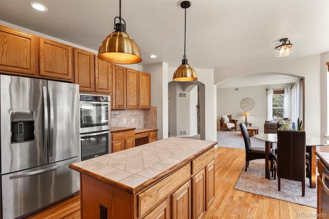 22386 E Arbor Pl, Aurora, CO 80016 - kitchen featuring appliances with stainless steel finishes, arched walkways, tile countertops, decorative backsplash, and light wood-style floors