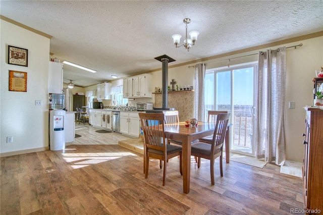 dining room featuring a wood stove, ceiling fan with notable chandelier, light wood-style floors, and a textured ceiling