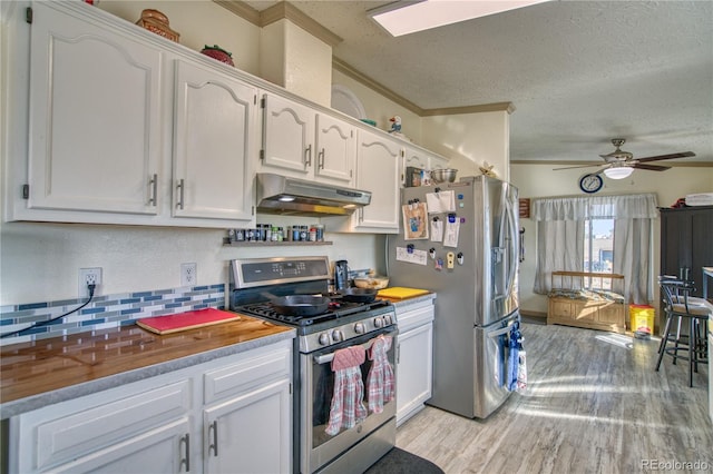 kitchen with a textured ceiling, under cabinet range hood, light wood finished floors, white cabinetry, and stainless steel appliances