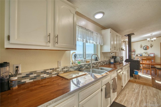 kitchen with a sink, decorative columns, a textured ceiling, crown molding, and light wood-style flooring