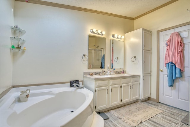 full bath with a sink, double vanity, a textured ceiling, crown molding, and a garden tub