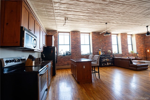 2261 Blake St Unit 5H, Denver, CO 80205 - kitchen featuring stainless steel appliances, brick wall, a breakfast bar, a kitchen island, and wood finished floors