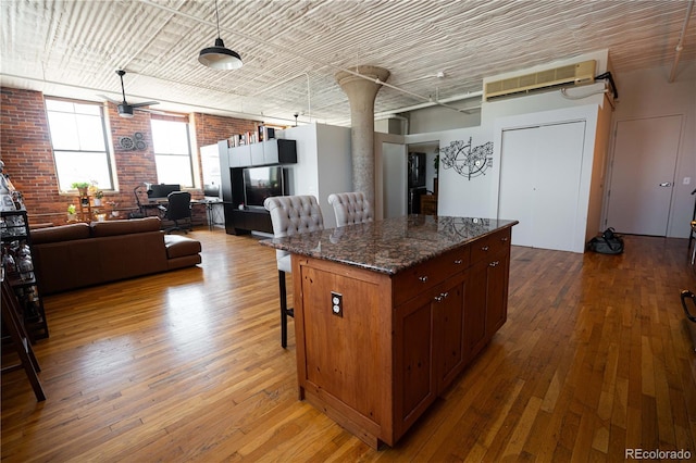 2261 Blake St Unit 5H, Denver, CO 80205 - kitchen with a kitchen breakfast bar, open floor plan, brick wall, wood-type flooring, and dark stone countertops