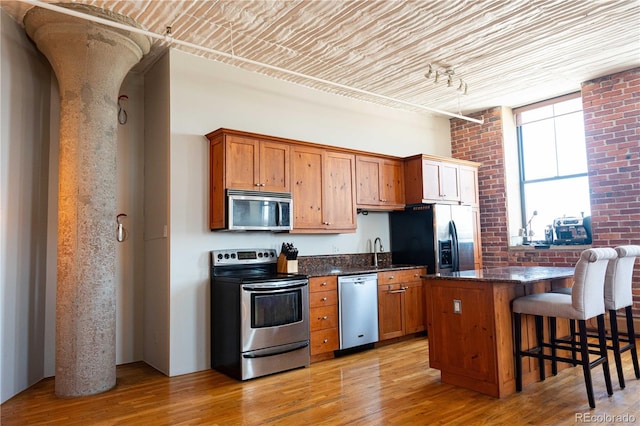 2261 Blake St Unit 5H, Denver, CO 80205 - kitchen with stainless steel appliances, a kitchen breakfast bar, light wood-type flooring, brown cabinetry, and brick wall