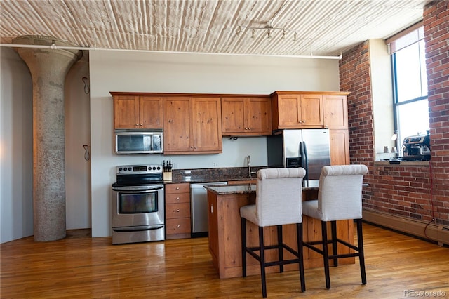 2261 Blake St Unit 5H, Denver, CO 80205 - kitchen featuring stainless steel appliances, brick wall, wood finished floors, a kitchen bar, and a center island