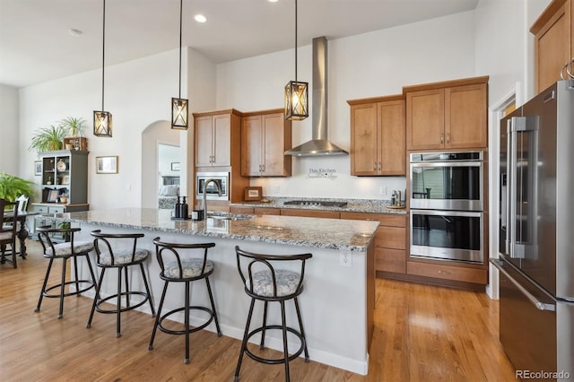 18926 W 94th Ave, Arvada, CO 80007 - kitchen with appliances with stainless steel finishes, wall chimney range hood, brown cabinetry, arched walkways, and light wood finished floors