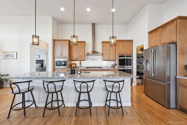 18926 W 94th Ave, Arvada, CO 80007 - kitchen with appliances with stainless steel finishes, wall chimney exhaust hood, a towering ceiling, light wood-style floors, and a kitchen bar