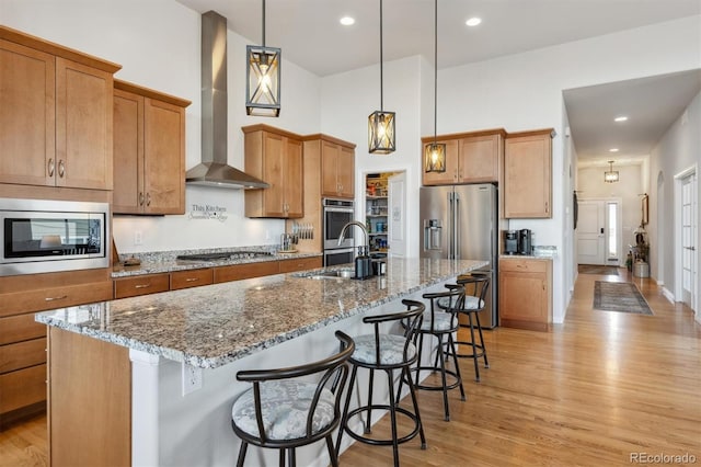 18926 W 94th Ave, Arvada, CO 80007 - kitchen with stainless steel appliances, wall chimney exhaust hood, light wood finished floors, a kitchen island with sink, and a high ceiling