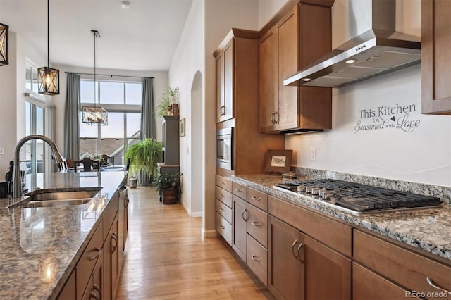 18926 W 94th Ave, Arvada, CO 80007 - kitchen featuring wall chimney exhaust hood, brown cabinetry, stainless steel appliances, light wood-style floors, and dark stone counters