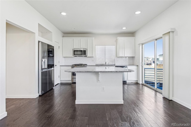 kitchen with a kitchen island, white cabinetry, backsplash, stainless steel appliances, and light stone countertops