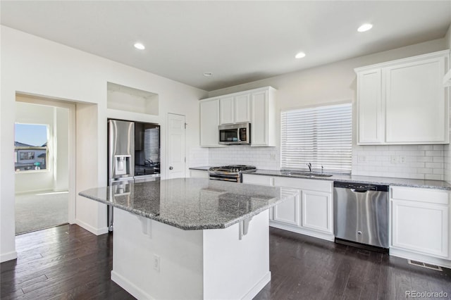 kitchen with dark stone countertops, stainless steel appliances, a kitchen island, and white cabinets