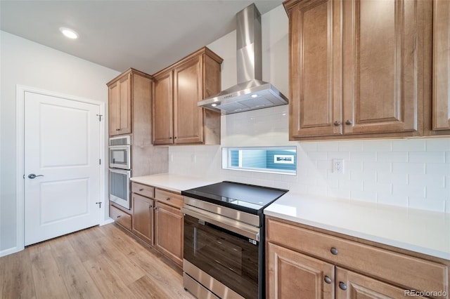 22384 E 49th Pl, Aurora, CO 80019 - kitchen featuring wall chimney range hood, stainless steel appliances, light wood-style flooring, and light countertops