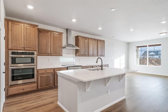 22384 E 49th Pl, Aurora, CO 80019 - kitchen with wall chimney range hood, appliances with stainless steel finishes, light wood-style flooring, a kitchen island with sink, and backsplash