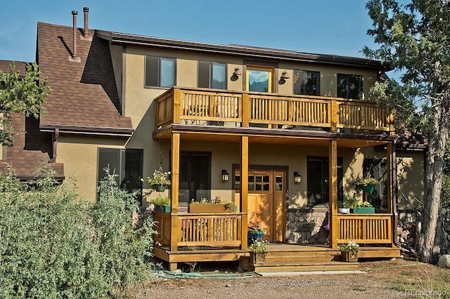 view of front facade with a balcony, roof with shingles, and stucco siding