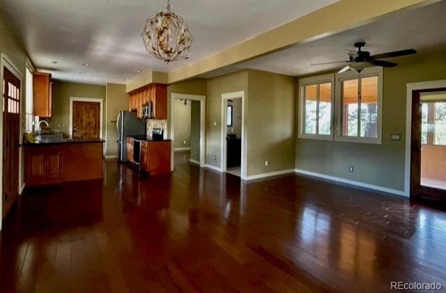 interior space with decorative light fixtures, kitchen peninsula, ceiling fan with notable chandelier, and dark hardwood / wood-style flooring