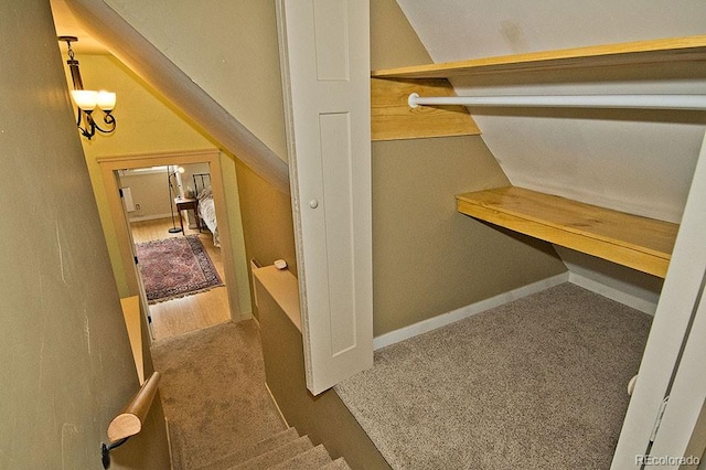 walk in closet with a chandelier, dark colored carpet, and vaulted ceiling