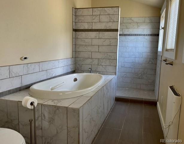 bathroom with tile floors, tiled tub, lofted ceiling, and toilet