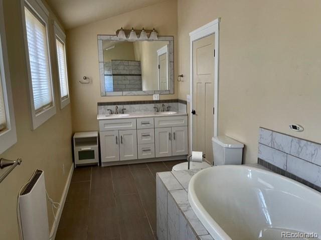 bathroom featuring a relaxing tiled bath, large vanity, dual sinks, and lofted ceiling