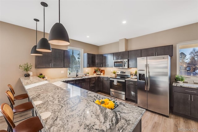 kitchen featuring dark brown cabinetry, decorative light fixtures, a kitchen bar, stainless steel appliances, and kitchen peninsula