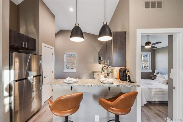 kitchen featuring a kitchen bar, light stone countertops, stainless steel refrigerator, dark brown cabinets, and vaulted ceiling