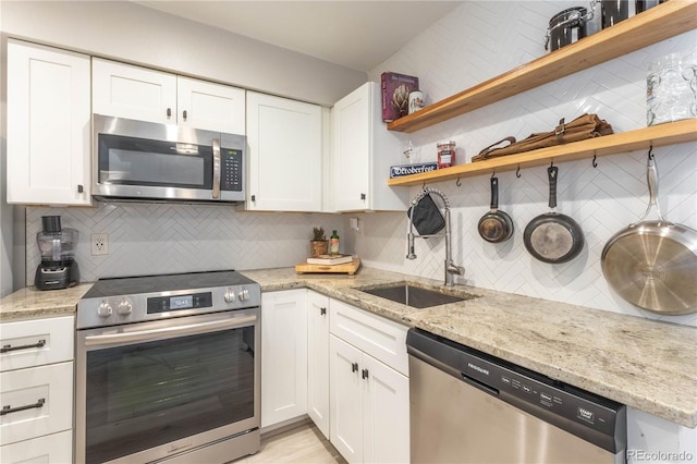 kitchen featuring backsplash, light stone counters, stainless steel appliances, sink, and white cabinetry