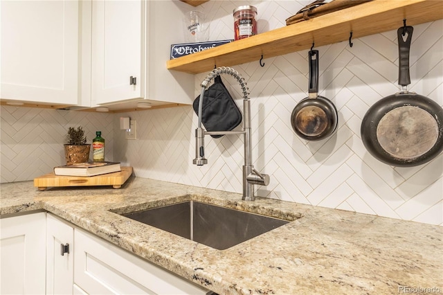 kitchen featuring white cabinets, backsplash, light stone counters, and sink