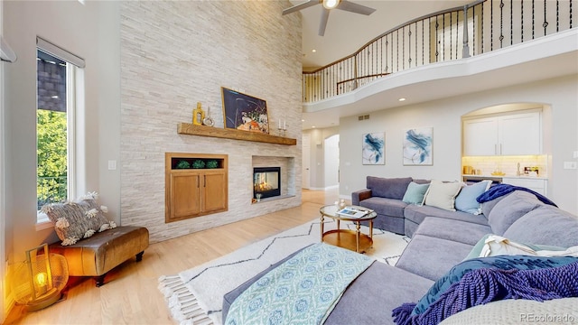 living room featuring a high ceiling, ceiling fan, a fireplace, and light wood-type flooring