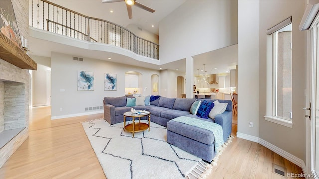 living room with a towering ceiling, a stone fireplace, ceiling fan, and light wood-type flooring