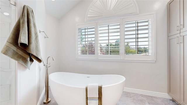 bathroom with tile patterned floors, a bathing tub, and vaulted ceiling