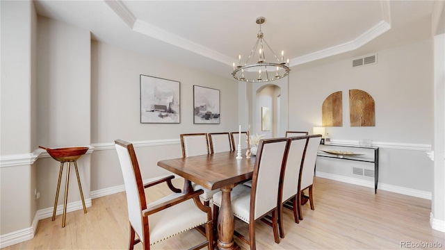 dining room featuring a raised ceiling, crown molding, a notable chandelier, and light hardwood / wood-style flooring